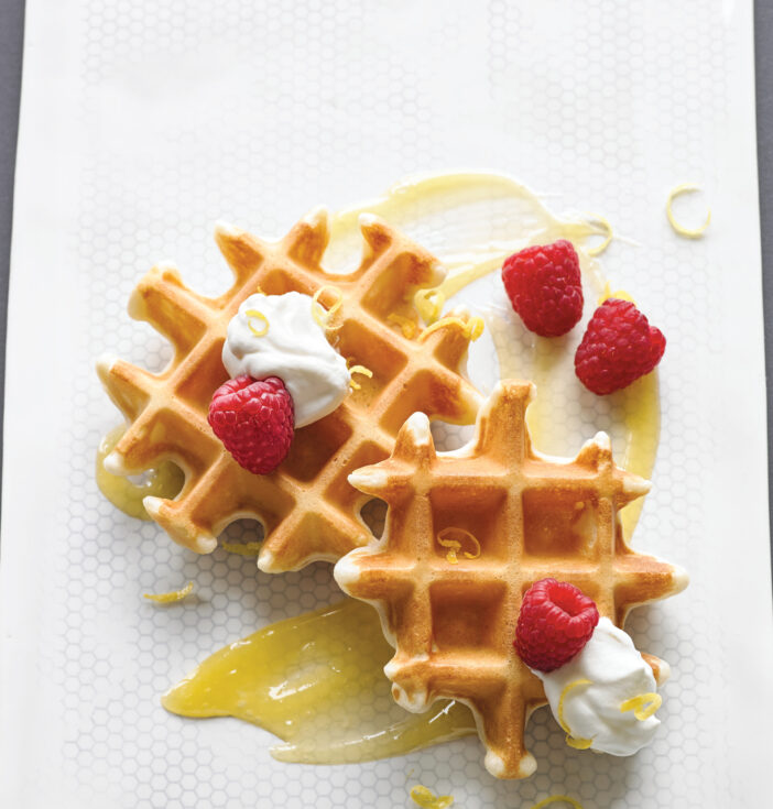 Waffles with cream and raspberries arranged on a white plate