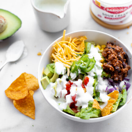 A bowl of taco salad, with chips, an avocado and sour cream