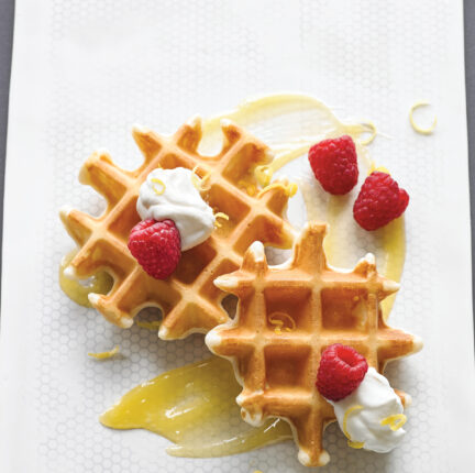 Waffles with cream and raspberries arranged on a white plate