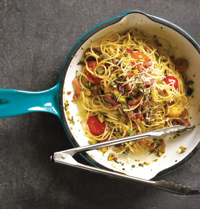 A blue cast iron pan with linguini dish and tongs