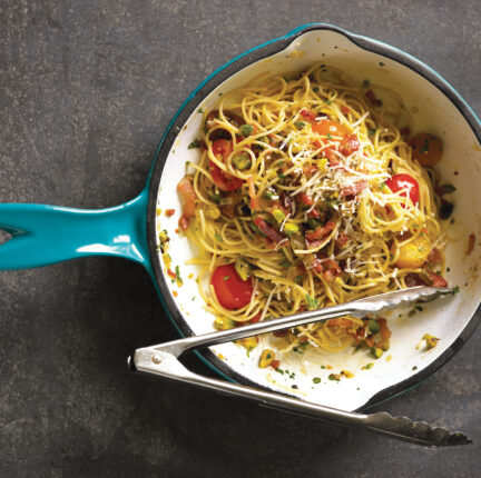 A blue cast iron pan with linguini dish and tongs